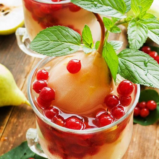 Poached pear dessert served in a glass cup with red currants and fresh mint leaves on a wooden table